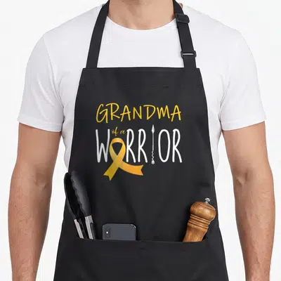 Childhood grandma apron - Stacked text GRANDMA of a WARRIOR with yellow ribbon and white arrow on grey background — shown on a black cotton canvas apron against a white background