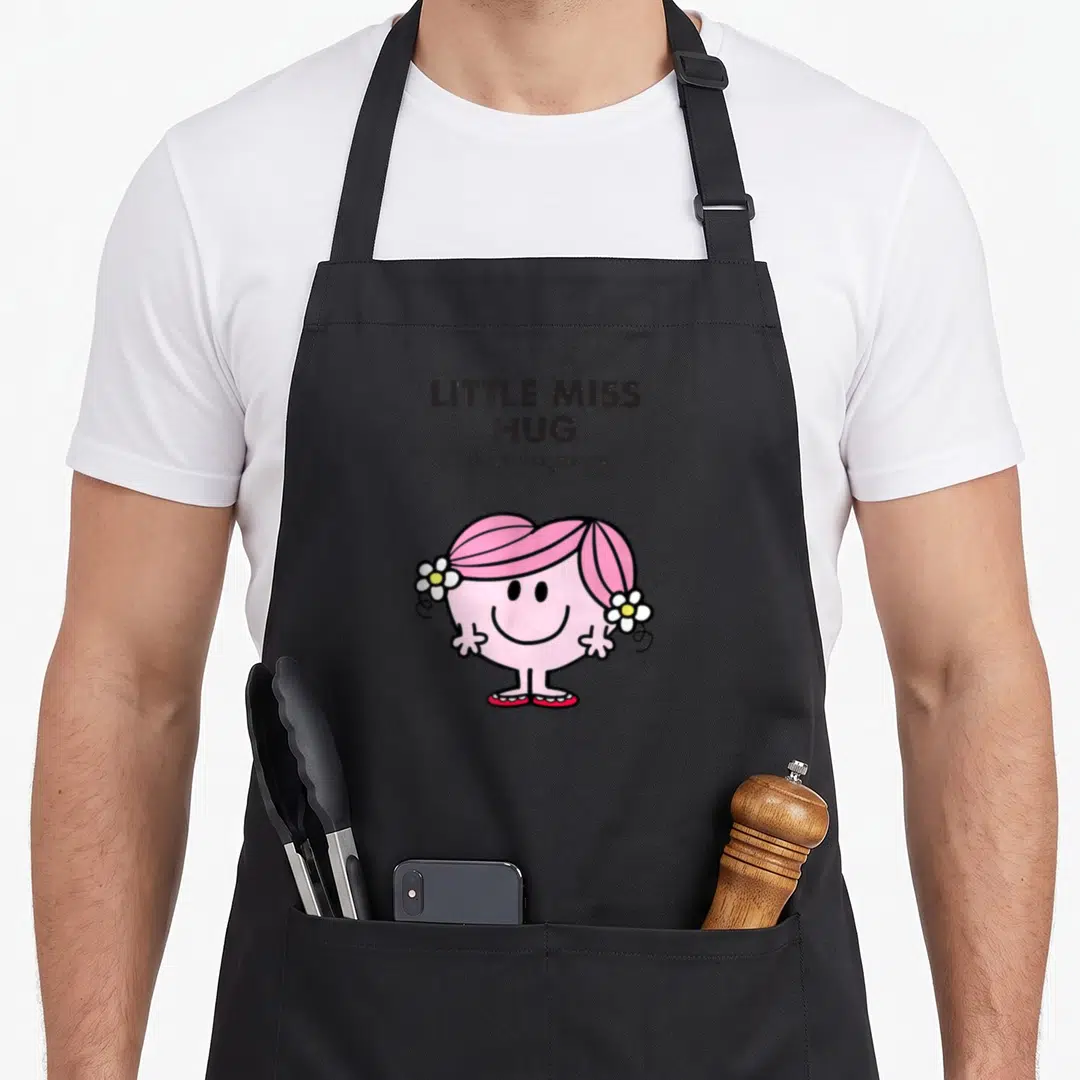 Hug mr apron - LITTLE MISS HUG text above pink cartoon character with white flowers and black outlines — shown on a black cotton canvas apron against a white background