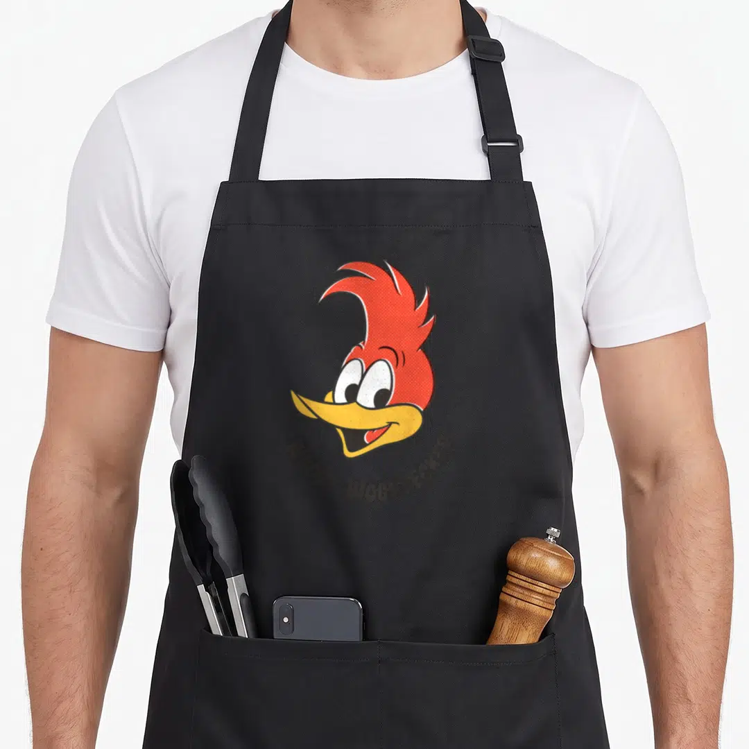 Smile woodpecker apron - Cartoon woodpecker head in red and yellow with curved WOODY WOODPECKER text below — shown on a black cotton canvas apron against a white background