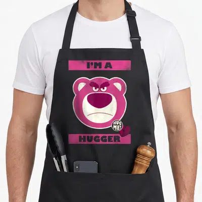 Lotso dog breed aprons - Angry pink bear face with I'm a Hugger text and broken heart icon — shown on a black cotton canvas apron against a white background