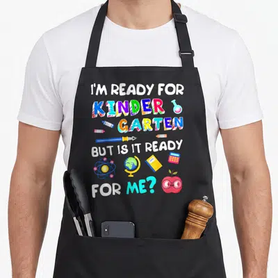 Funny 1st kindergarten apron - Stacked text I'm ready for kinder garten but is it ready for me with colorful crayons — shown on a black cotton canvas apron against a white background