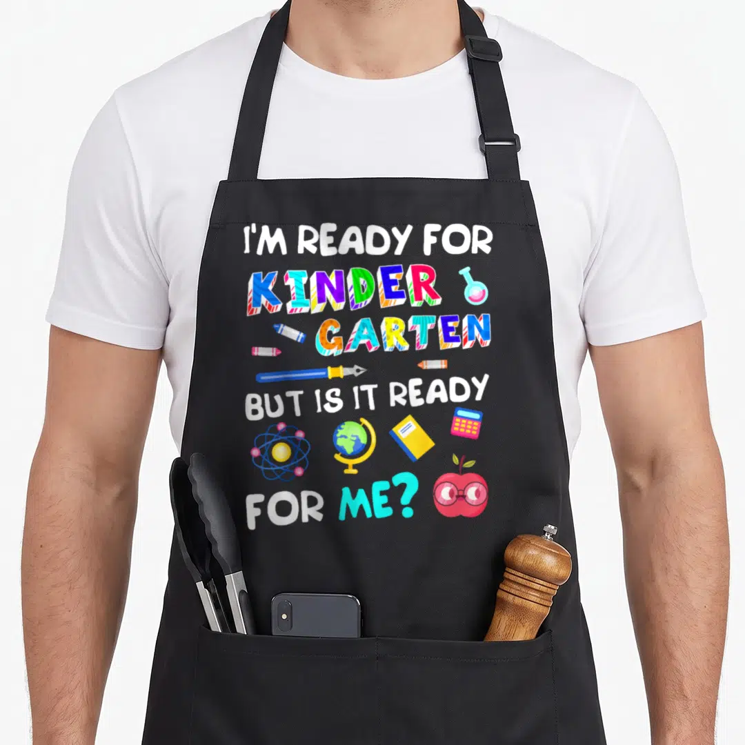 Funny 1st kindergarten apron - Stacked text I'm ready for kinder garten but is it ready for me with colorful crayons — shown on a black cotton canvas apron against a white background