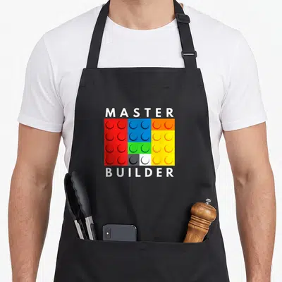 Master block & apron - MASTER and BUILDER text surrounding a grid of red, blue, yellow, green, white, and orange — shown on a black cotton canvas apron against a white background