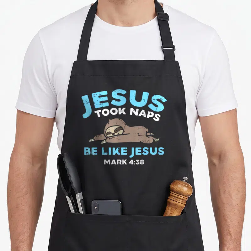 Took bible verse apron - Cartoon brown sloth sleeping under JESUS TOOK NAPS text in blue and white — shown on a black cotton canvas apron against a white background