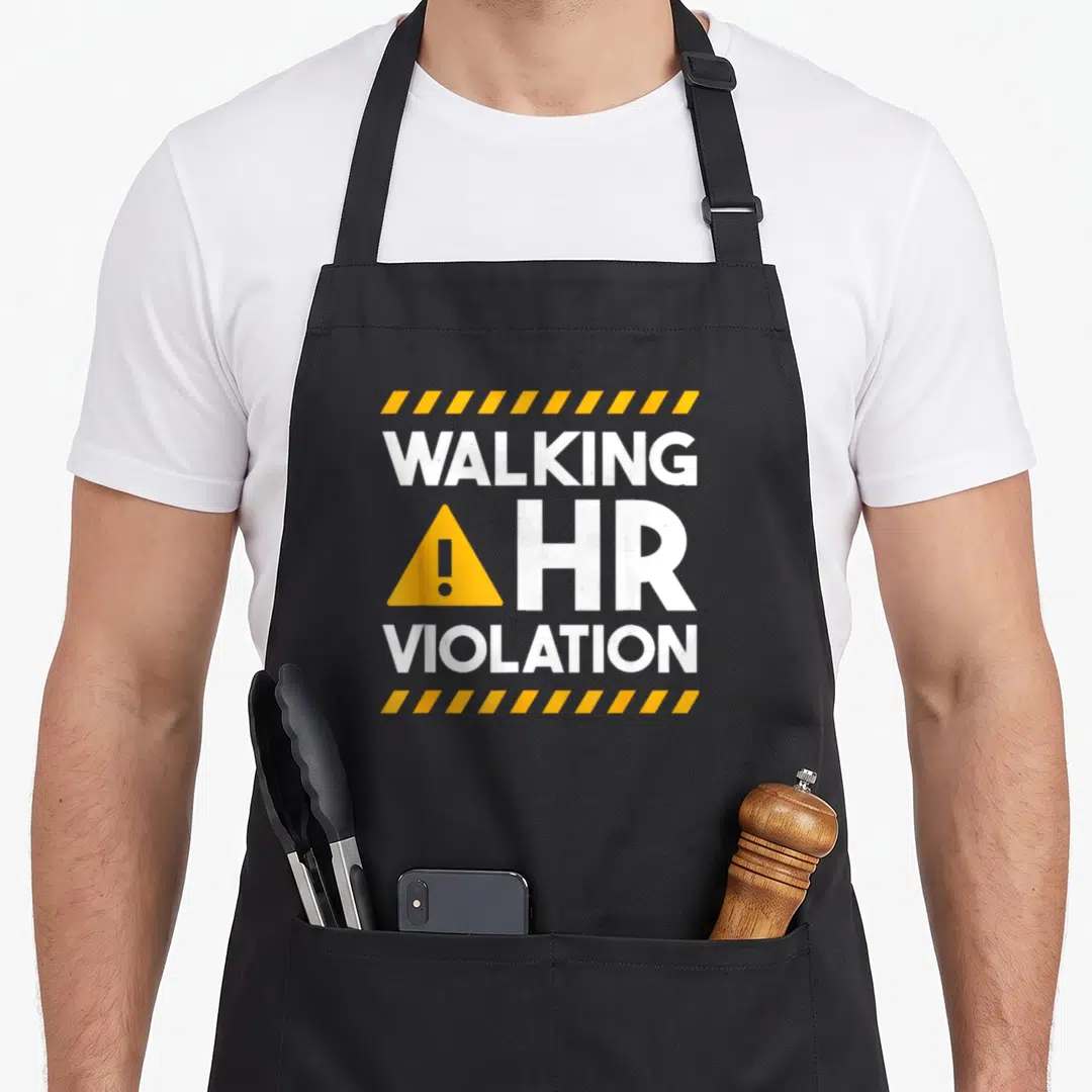 Human walking apron - WALKING HR VIOLATION text with yellow warning triangle and hazard stripes on grey — shown on a black cotton canvas apron against a white background