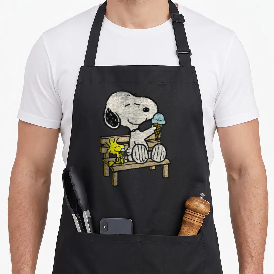 Woodstock bench apron - Snoopy and Woodstock eating ice cream on a wooden bench in distressed style — shown on a black cotton canvas apron against a white background