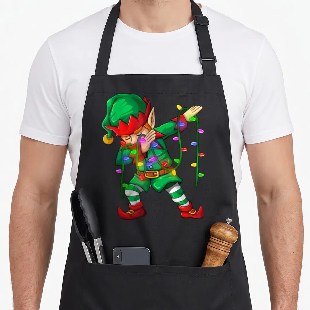 Costume christmas elf apron - Cartoon elf dabbing tangled in green string lights with red, yellow, blue, and pink bulbs — shown on a black cotton canvas apron against a white background