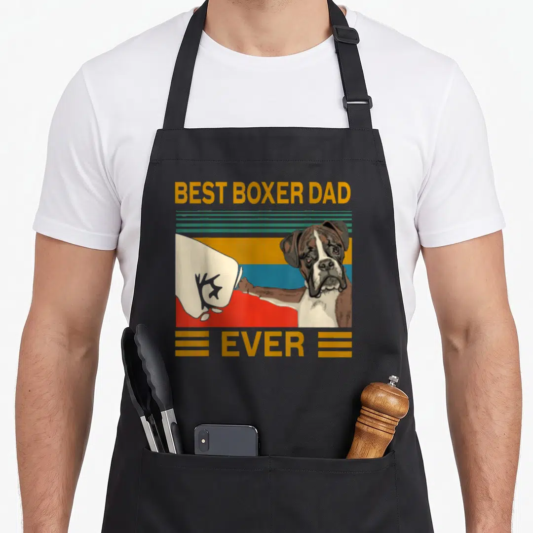 Bump boxer dog apron - Cartoon boxer dog fist bumping glove with BEST BOXER DAD EVER text on striped background — shown on a black cotton canvas apron against a white background