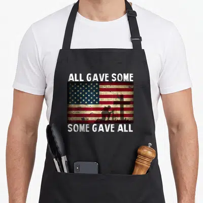 Gave retired soldier apron - Distressed USA flag with kneeling soldier silhouette and cross, text All Gave Some Some — shown on a black cotton canvas apron against a white background
