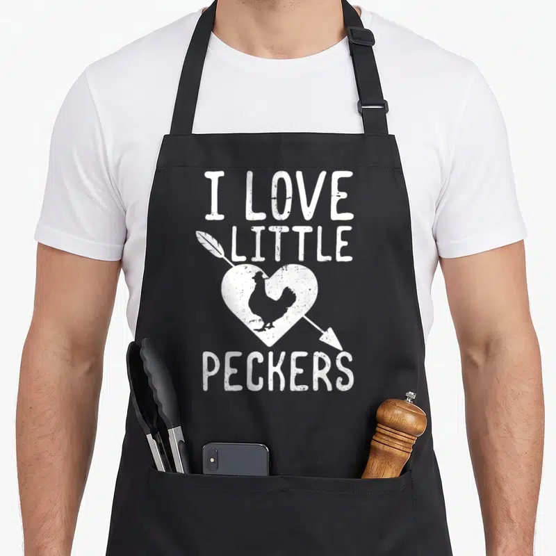 Funny pecker chicken apron - White distressed text I LOVE LITTLE PECKERS with chicken inside pierced heart — shown on a black cotton canvas apron against a white background