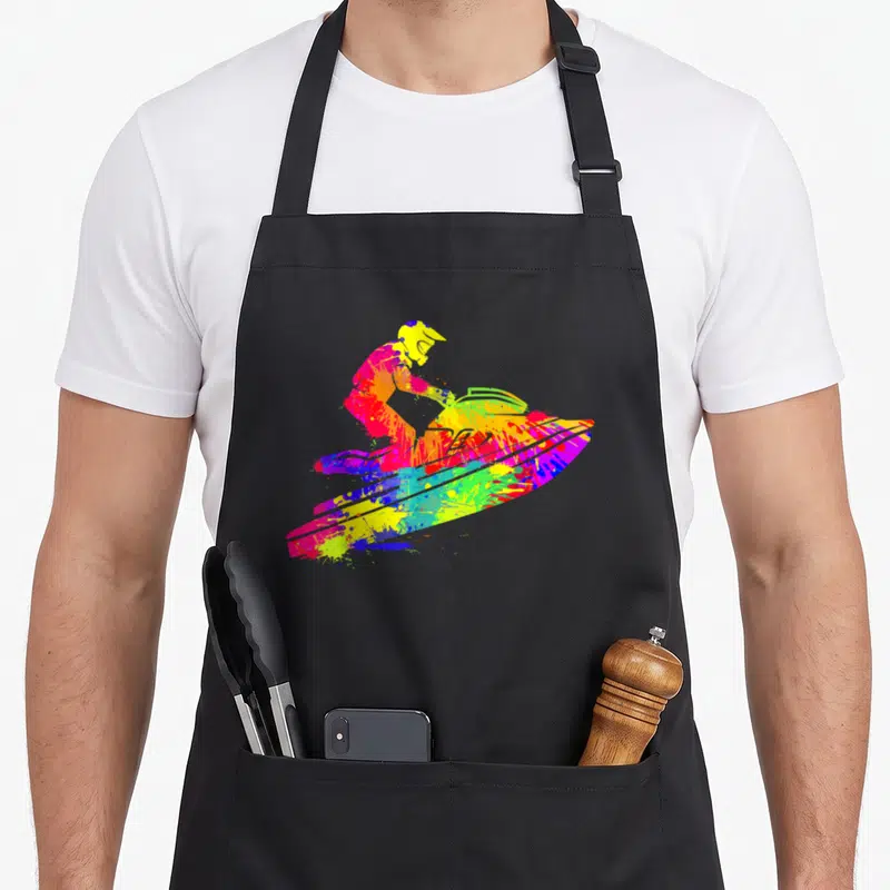 Sport jet girl apron - Multi-colored tie-dye splatter silhouette of a person riding a jet ski — shown on a black cotton canvas apron against a white background