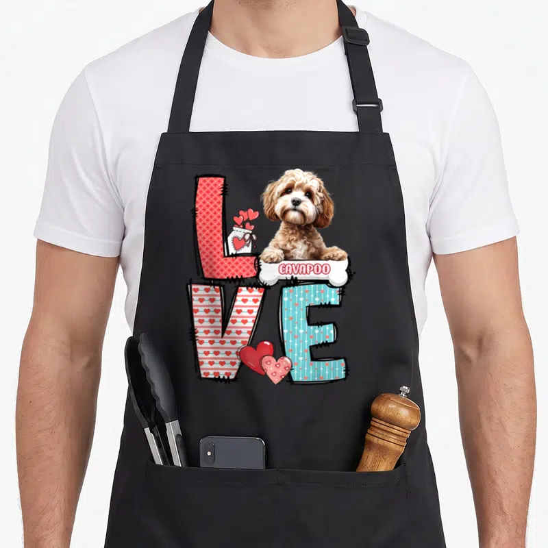 Cavapoo valentine's day apron - LOVE letters with heart patterns and Cavapoo dog on bone labeled CAVAPOO — shown on a black cotton canvas apron against a white background