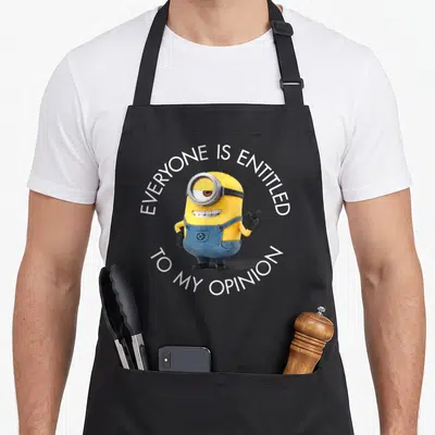 Stuart despicable me apron - Yellow minion with blue overalls and circular white text reading EVERYONE IS ENTITLED — shown on a black cotton canvas apron against a white background