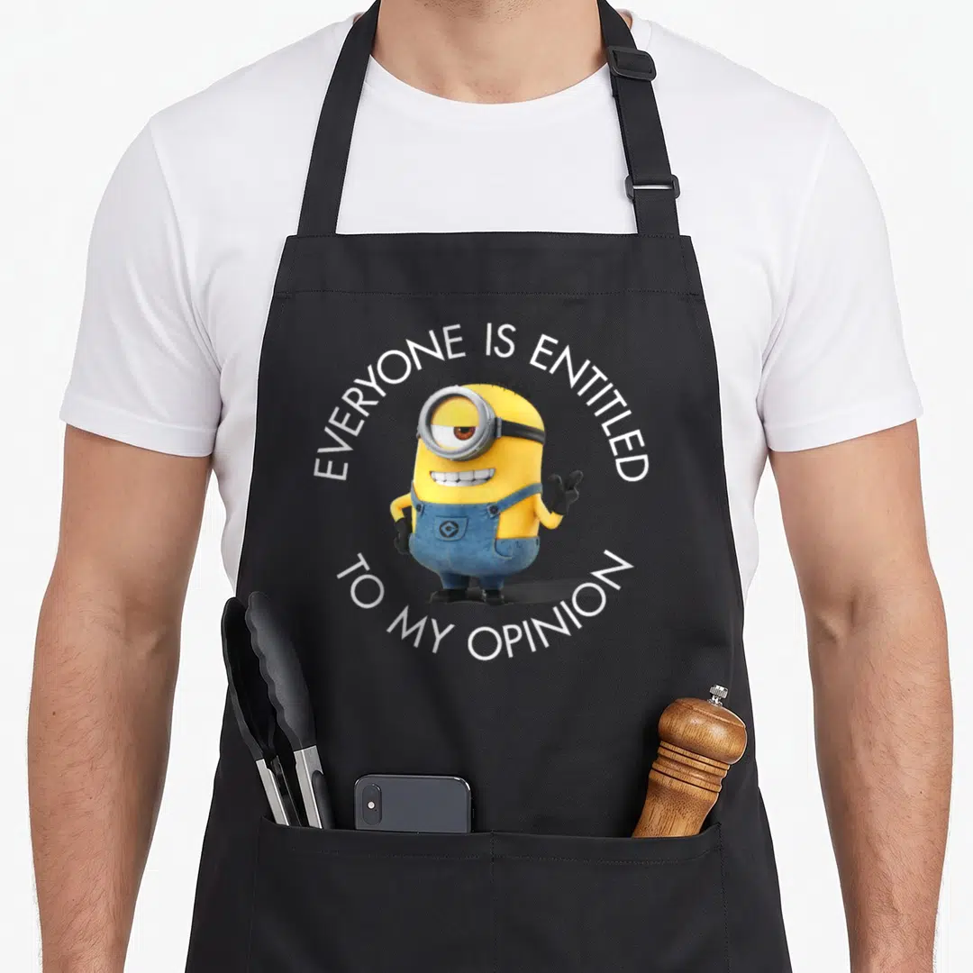 Stuart despicable me apron - Yellow minion with blue overalls and circular white text reading EVERYONE IS ENTITLED — shown on a black cotton canvas apron against a white background