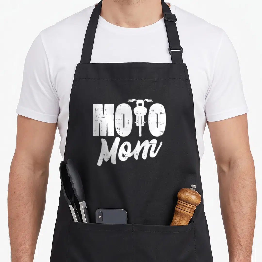 Moto motorcycle aprons - White distressed MOTO Mom text with motorcycle silhouette replacing the letter T — shown on a black cotton canvas apron against a white background