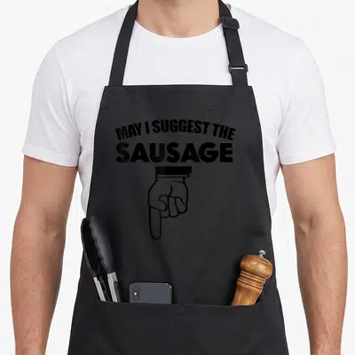 May suggest sausage apron - Black text reading MAY I SUGGEST THE SAUSAGE above a pointing cartoon hand — shown on a black cotton canvas apron against a white background