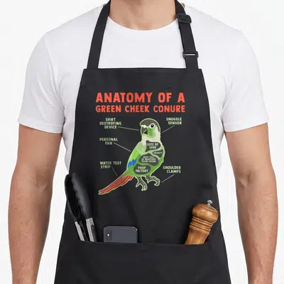 Pineapple bird apron - Cartoon green cheek conure labeled with humorous anatomical terms in red and green text — shown on a black cotton canvas apron against a white background