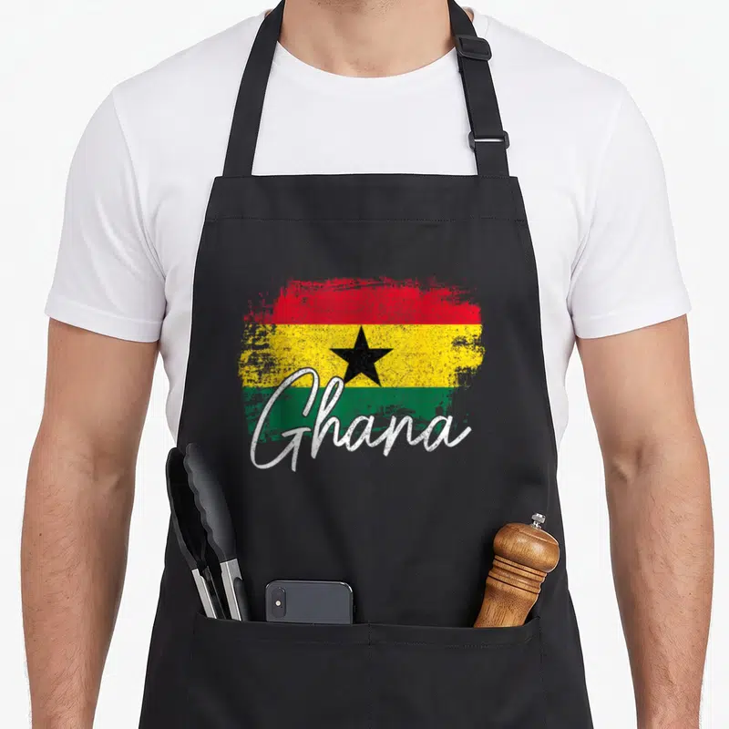 Ghana pride apron - Distressed Ghana flag with red yellow green stripes black star and white script text — shown on a black cotton canvas apron against a white background