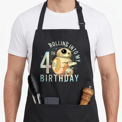 Rolling 4th birthday apron - BB-8 droid with ROLLING INTO MY 4TH BIRTHDAY text in white orange blue cartoon style — shown on a black cotton canvas apron against a white background