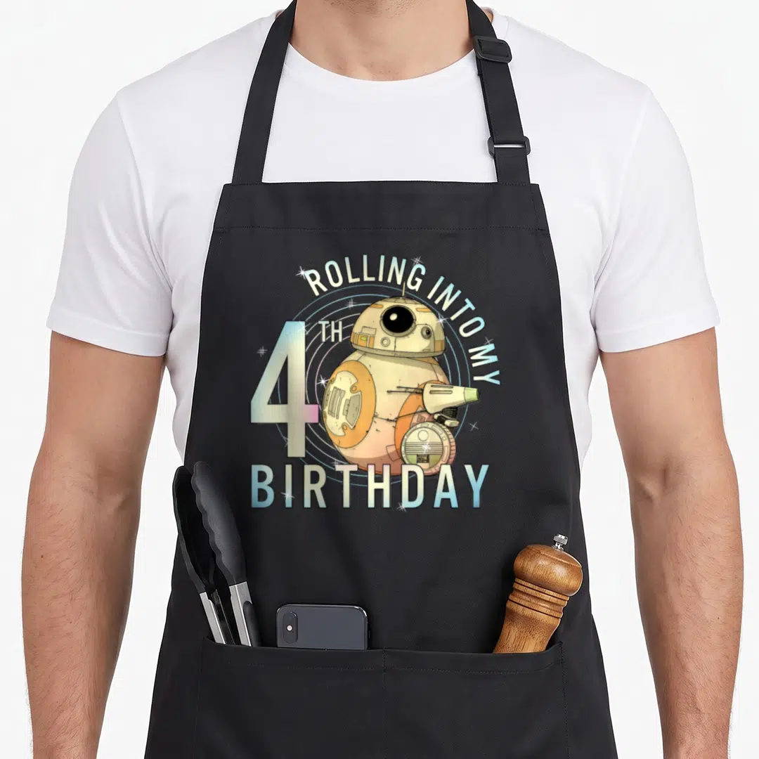 Rolling 4th birthday apron - BB-8 droid with ROLLING INTO MY 4TH BIRTHDAY text in white orange blue cartoon style — shown on a black cotton canvas apron against a white background