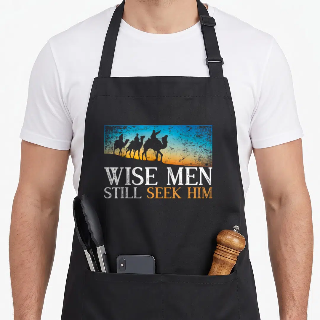 Desert christian apron - Retro silhouettes of three figures on camels above Wise Men Still Seek Him text in white — shown on a black cotton canvas apron against a white background