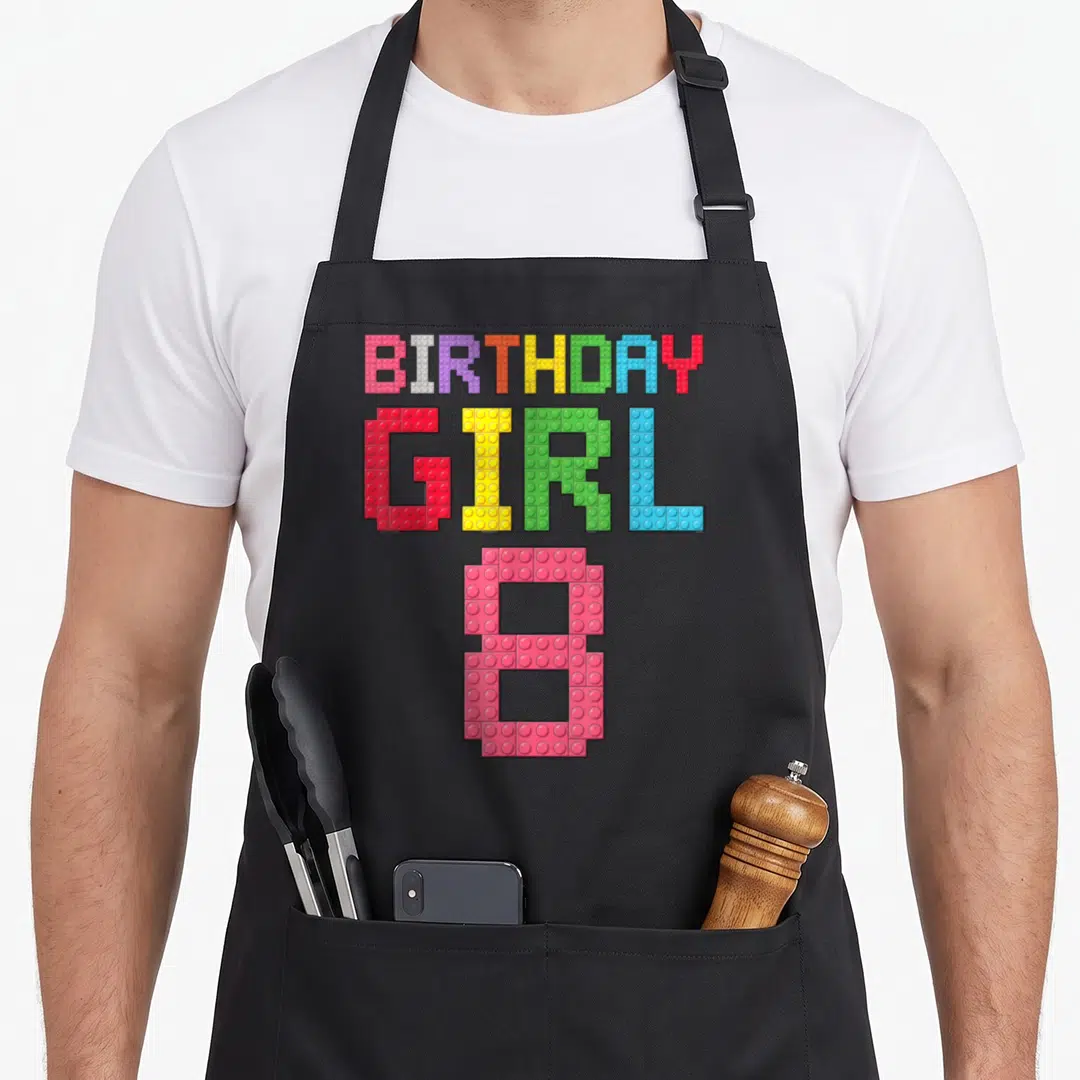 8th birthday grill master apron - BIRTHDAY GIRL 8 text designed as colorful cartoon plastic building bricks — shown on a black cotton canvas apron against a white background