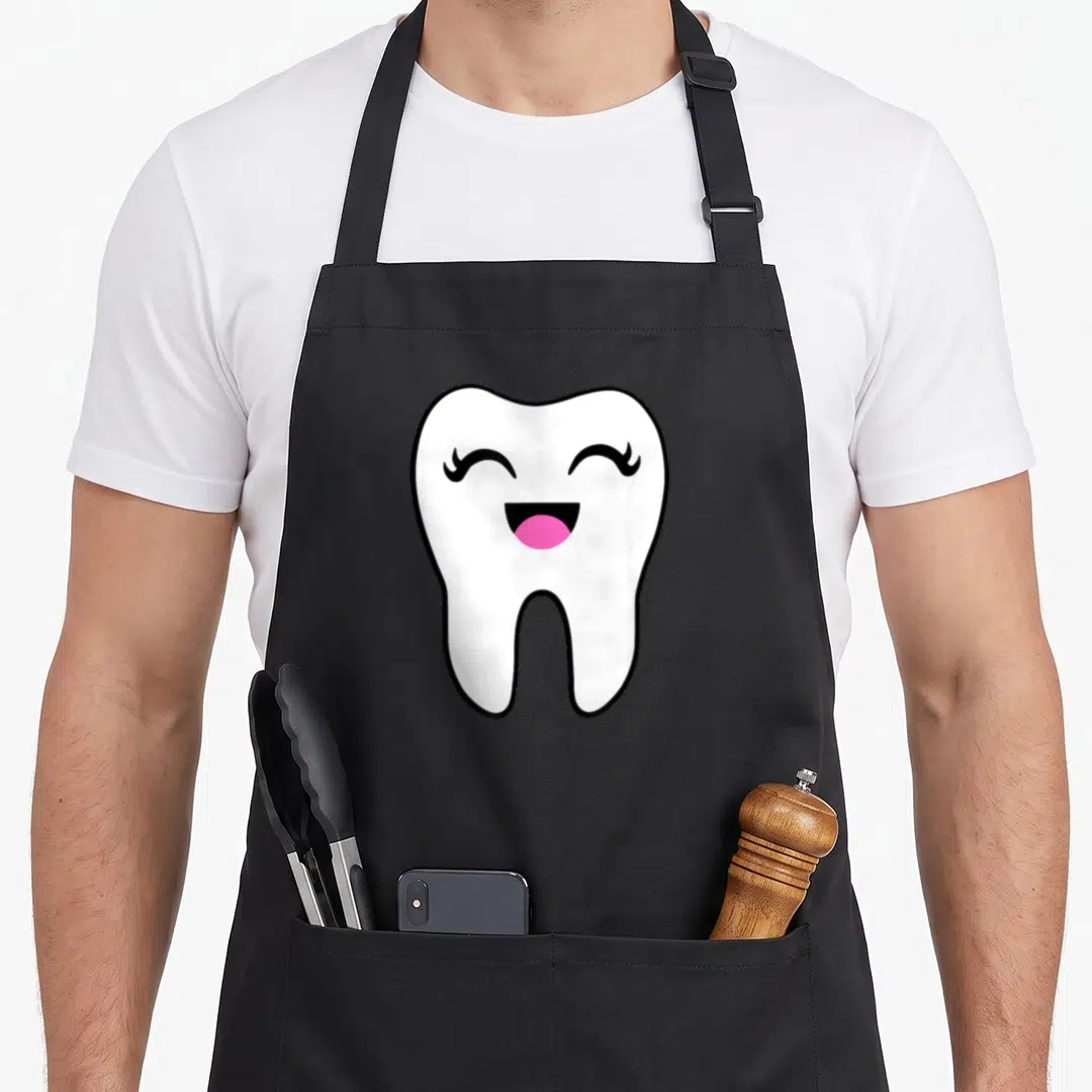 Tooth halloween apron - Cartoon white tooth with smiling face, black outline, and pink tongue on black background — shown on a black cotton canvas apron against a white background