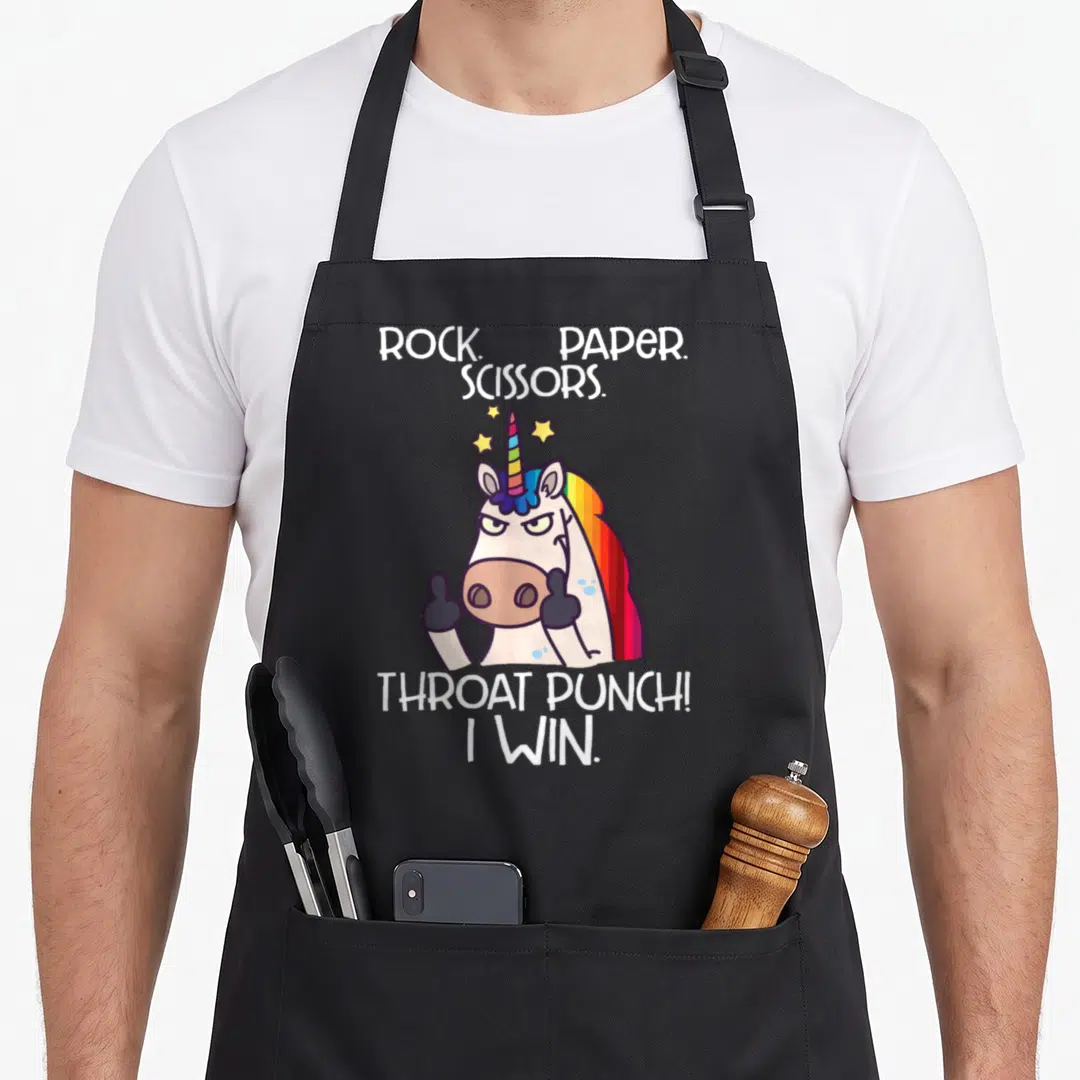 Win paper apron - Cartoon unicorn giving thumbs up with Rock Paper Scissors Throat Punch text and stars — shown on a black cotton canvas apron against a white background