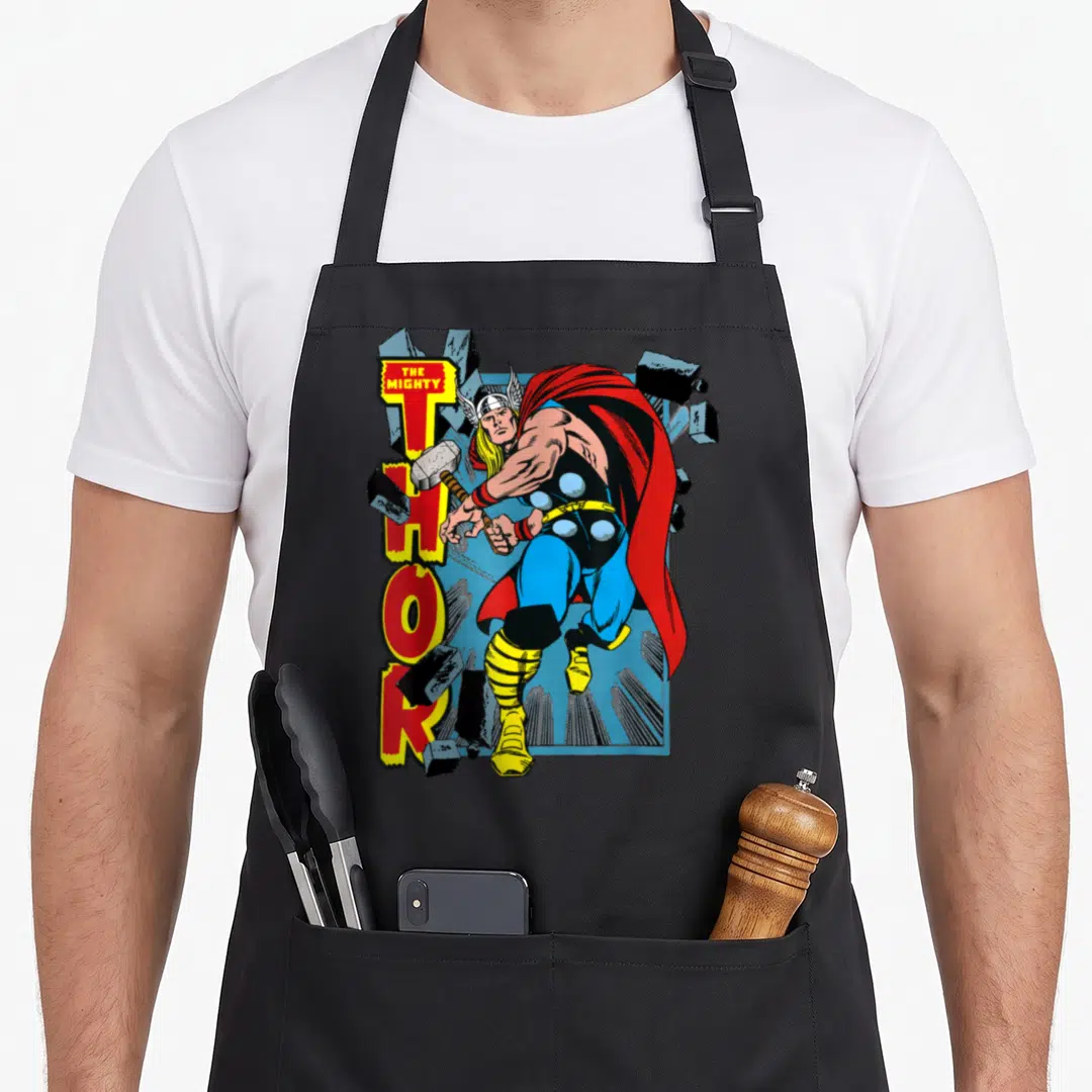 Mighty break apron - Thor breaking through grey rocks next to red and yellow vertical text — shown on a black cotton canvas apron against a white background