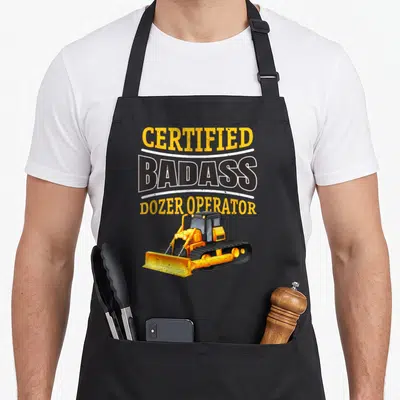 Dozer heavy canvas aprons - Stacked CERTIFIED BADASS DOZER OPERATOR text above yellow cartoon bulldozer on grey — shown on a black cotton canvas apron against a white background