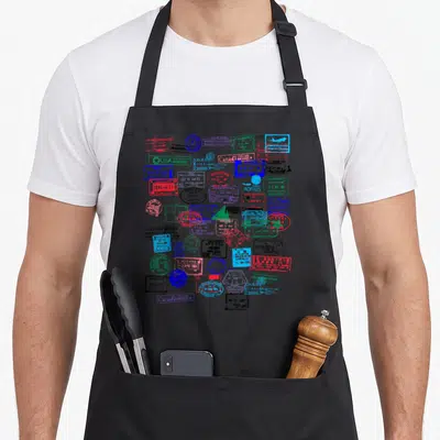 Passport travel aprons - Scattered cluster of red, blue, green, and black passport stamps and travel icons — shown on a black cotton canvas apron against a white background