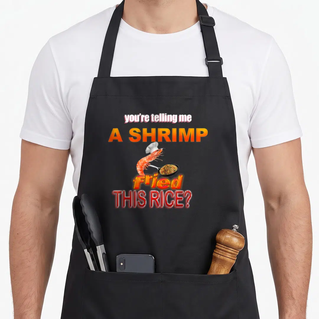 Telling meme apron - Cartoon shrimp in chef hat holding frying pan with stacked text you're telling me a shrimp fried — shown on a black cotton canvas apron against a white background
