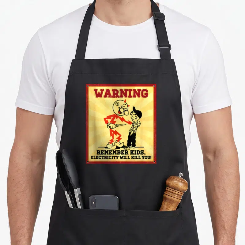 Remember electrician apron - Vintage warning sign with electric monster holding knife and boy, red border — shown on a black cotton canvas apron against a white background