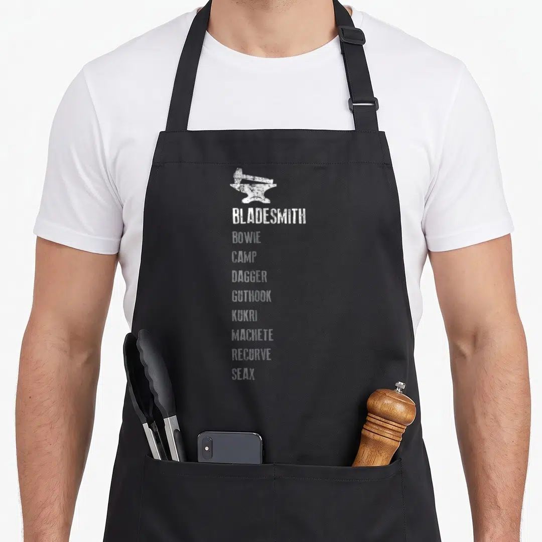Bladesmith blacksmith apron - White anvil hammer and vertical list of knife names like Bowie and Kukri in distressed — shown on a black cotton canvas apron against a white background