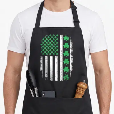 Shamrock st patrick day aprons - Distressed US flag with green shamrock grid and vertical white stripes — shown on a black cotton canvas apron against a white background