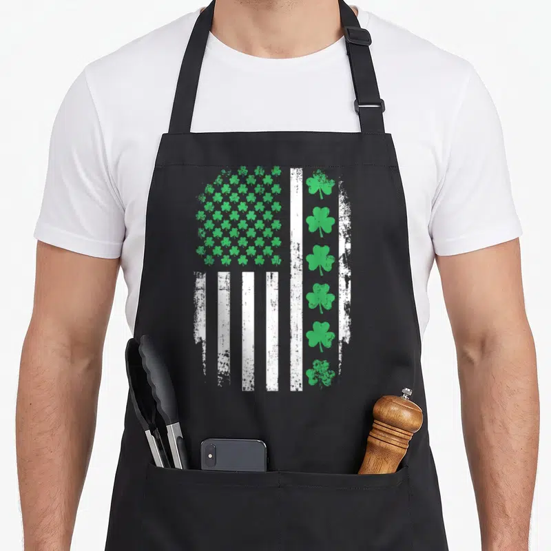 Shamrock st patrick day aprons - Distressed US flag with green shamrock grid and vertical white stripes — shown on a black cotton canvas apron against a white background