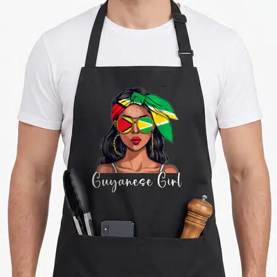 Souvenir guyana apron - Woman portrait with flag sunglasses and headscarf and Guyanese Girl text — shown on a black cotton canvas apron against a white background
