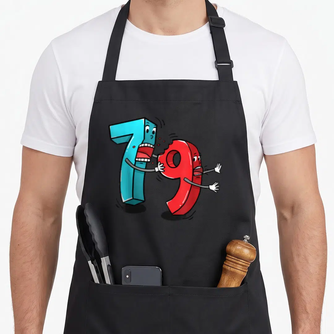Ate math apron - Light blue 7 biting red 9 cartoon digits with arms legs and faces — shown on a black cotton canvas apron against a white background