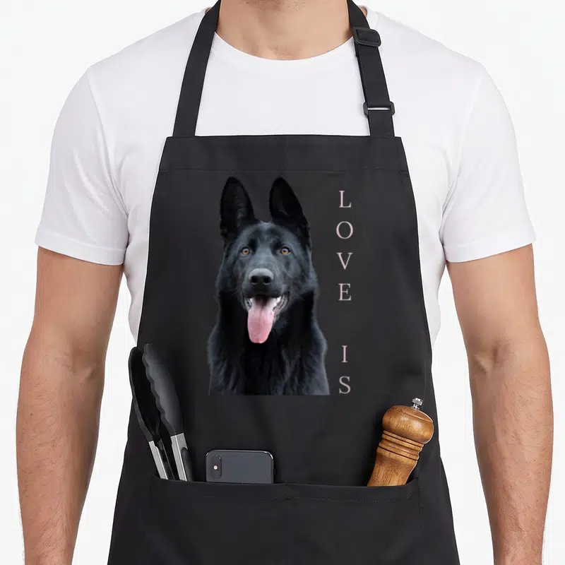 German shepherd shepard dog apron - Black German Shepherd photo with vertical LOVE IS text in light purple — shown on a black cotton canvas apron against a white background
