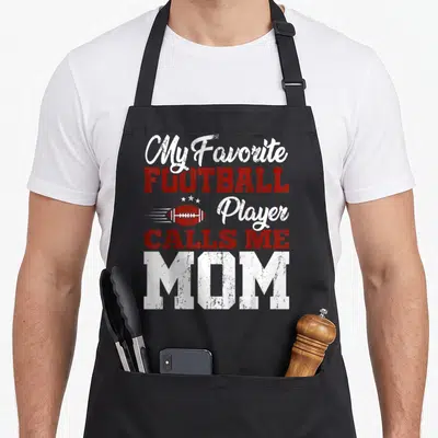 Football mother's day aprons - Distressed red and white text My Favorite Football Player Calls Me Mom with football — shown on a black cotton canvas apron against a white background