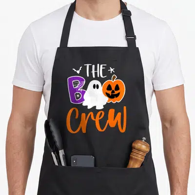 Crew halloween apron - Cartoon ghost and pumpkin flanking purple B spelling BOO Crew — shown on a black cotton canvas apron against a white background