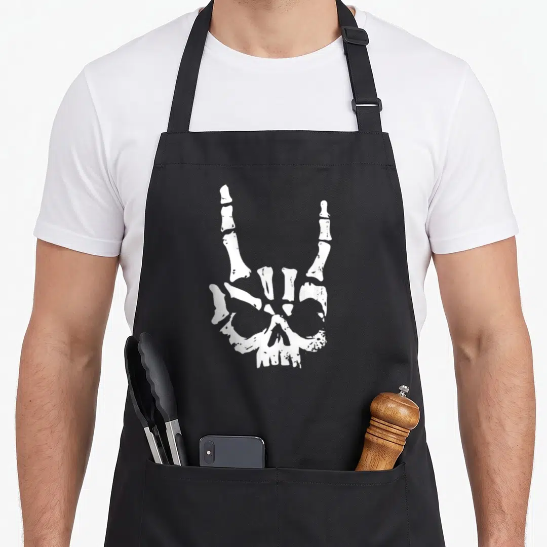 Rocker heavy metal apron - White line art of skeletal hand above skull making rock on sign — shown on a black cotton canvas apron against a white background
