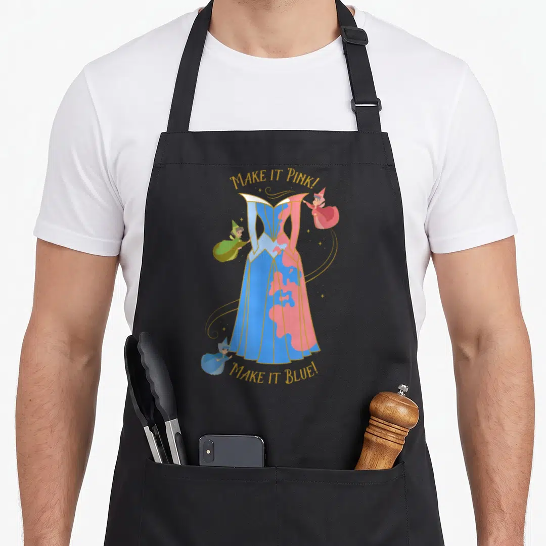 65th beauty apron - Split blue and pink dress with three fairies and gold text arched above and below — shown on a black cotton canvas apron against a white background