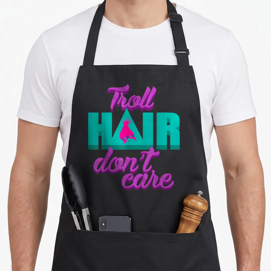 Troll messy aprons - Purple and teal text reading Troll Hair Don't Care with a pink tuft inside the letter — shown on a black cotton canvas apron against a white background