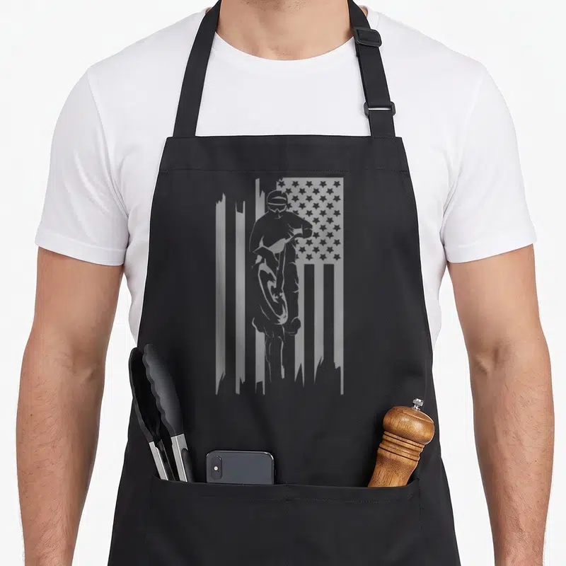 Motocross dirt american flag apron - Grey silhouette of a motocross rider inside a distressed American flag pattern — shown on a black cotton canvas apron against a white background