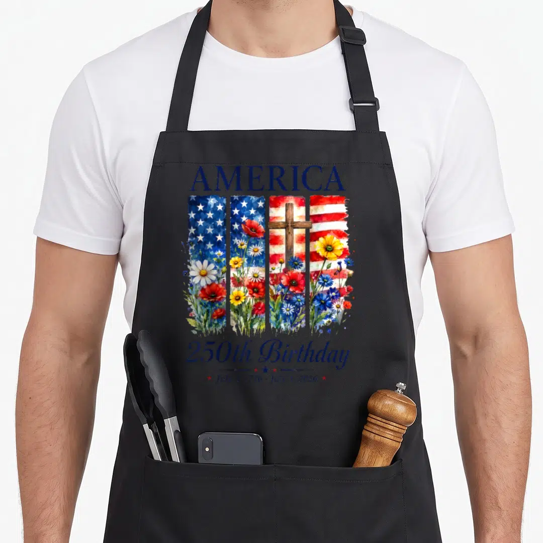 250th floral aprons - Watercolor USA flag with brown cross and wildflowers reading AMERICA 250th Birthday July 4 1776 — shown on a black cotton canvas apron against a white background