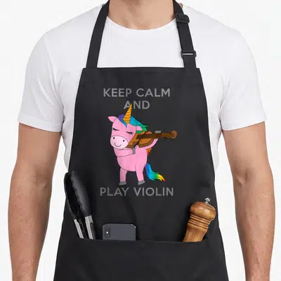 Play unicorn apron - Pink cartoon unicorn playing brown violin with grey hooves and text KEEP CALM AND PLAY VIOLIN — shown on a black cotton canvas apron against a white background