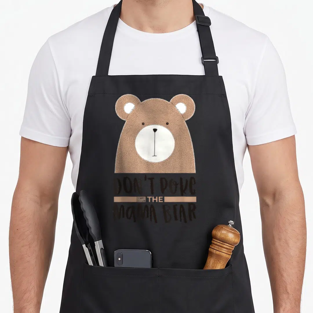Poke mother's day aprons - Cartoon brown bear head above stacked text Don't Poke the Mama Bear with tan banner — shown on a black cotton canvas apron against a white background