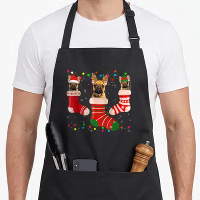 French womens christmas aprons - Three brown Frenchies in red and green stockings with colorful lights and snowflakes — shown on a black cotton canvas apron against a white background