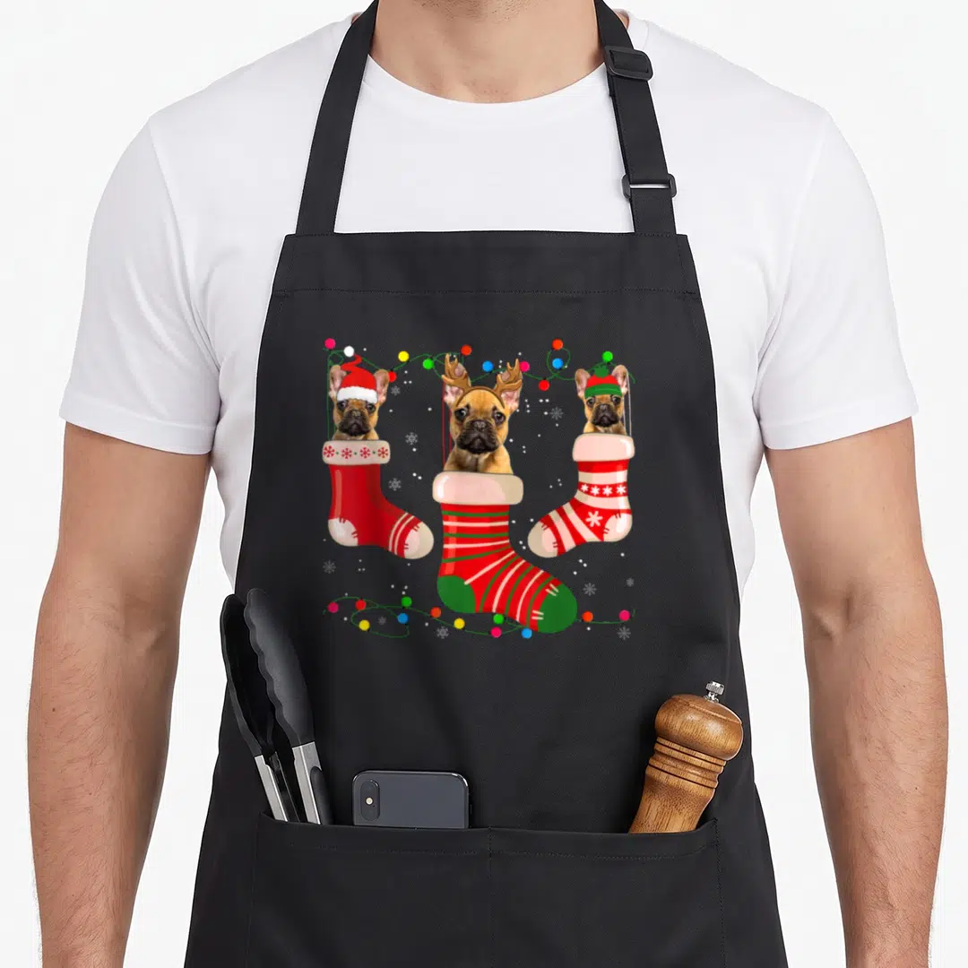 French womens christmas aprons - Three brown Frenchies in red and green stockings with colorful lights and snowflakes — shown on a black cotton canvas apron against a white background